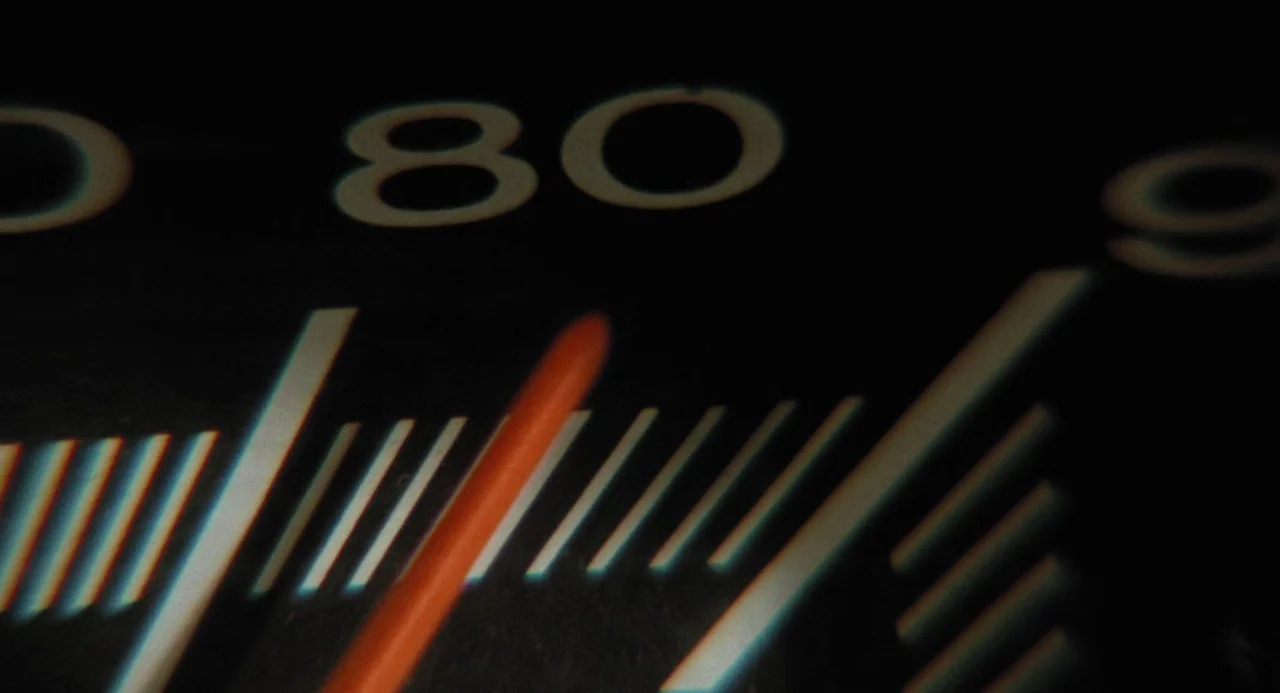 Duel (1971) movie still: closeup — A close-up of a vehicle speedometer dial features the number eighty and indicator marks. A blurred red needle…