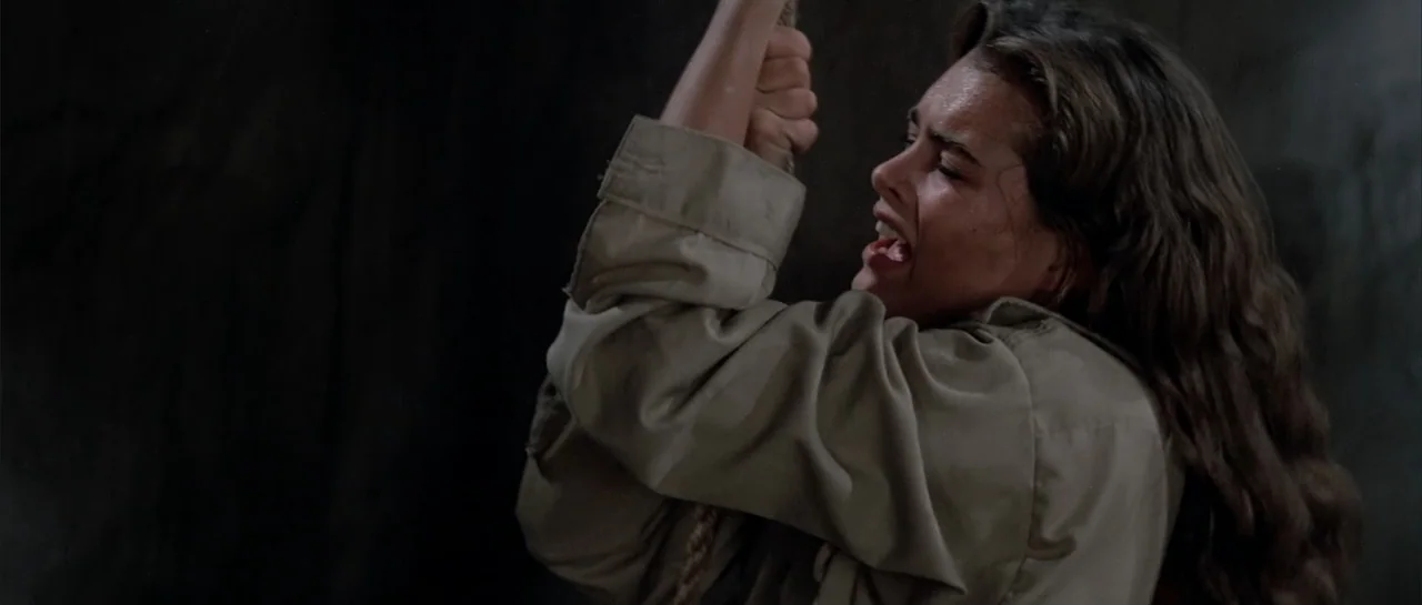Sahara (1995) movie still: medium — A dimly lit cave interior provides a dark backdrop for the subject. A woman pulls hard on a thick rope while her…