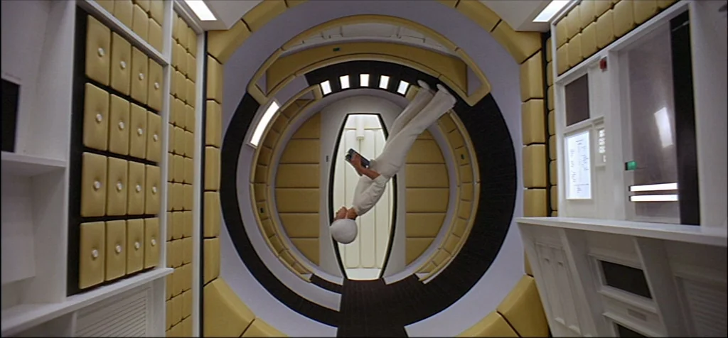 2001: A Space Odyssey (1968) movie still: wide — A circular, padded corridor in a futuristic spacecraft features white walls and yellow upholstery.…