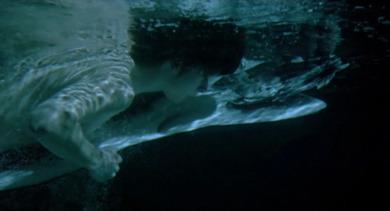 Deep End (1970) movie still: medium — A person swims beneath the surface of dark, murky water at night. Sunlight or moonlight filters from above,…
