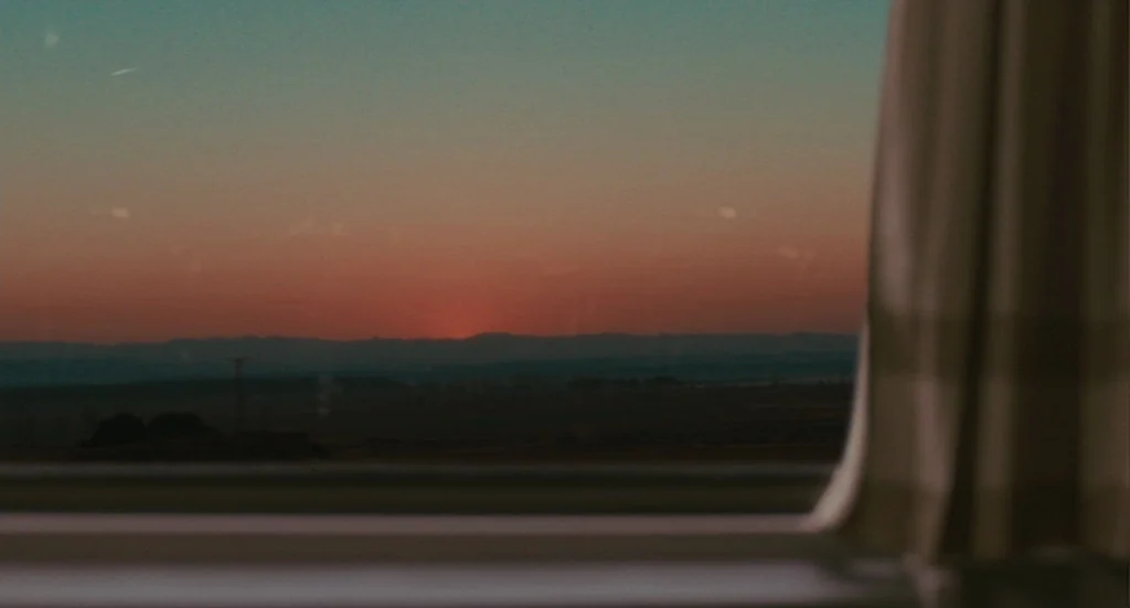 The Limits of Control (2009) movie still: establishing — A view through a train window looking out over a dark landscape at twilight. The sun dips…