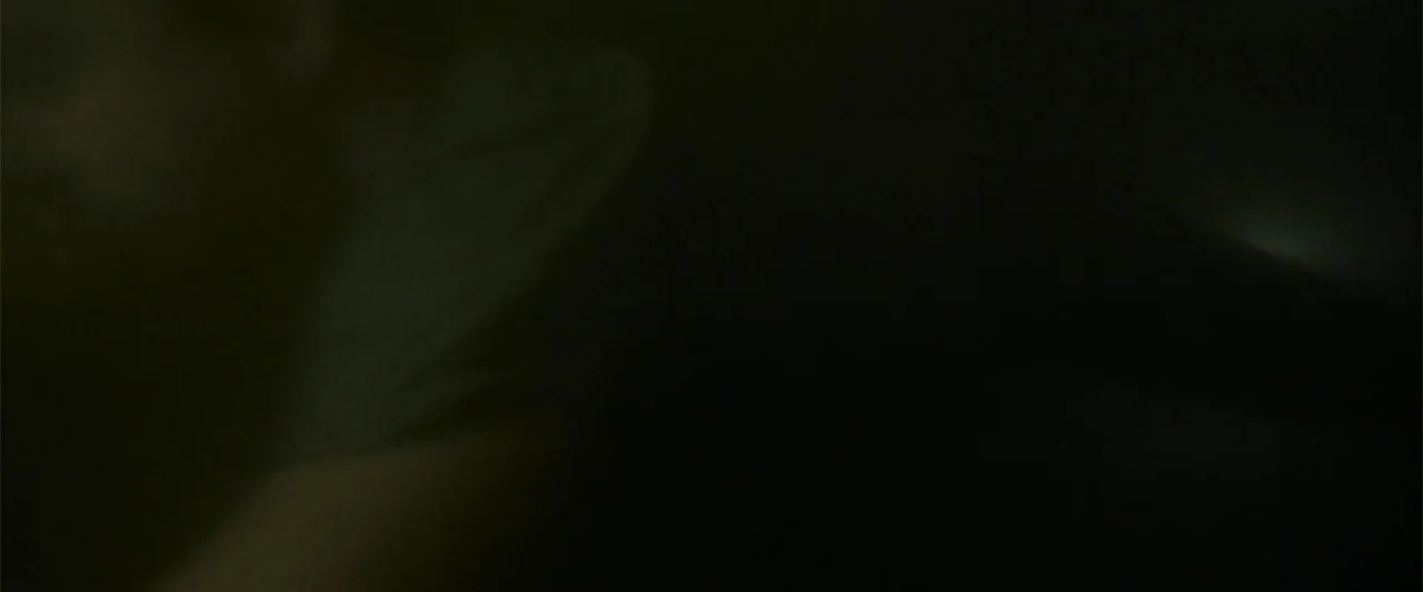 Black Water: Abyss (2020) movie still: closeup — A dark, minimally lit interior space features a person resting in shadow. The subject lies sideways…