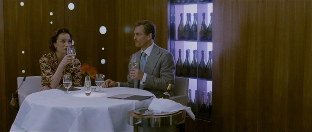 The Walker (2007) movie still: medium — A fine dining room with wood-paneled walls and an illuminated display of wine bottles. A man and a woman sit…