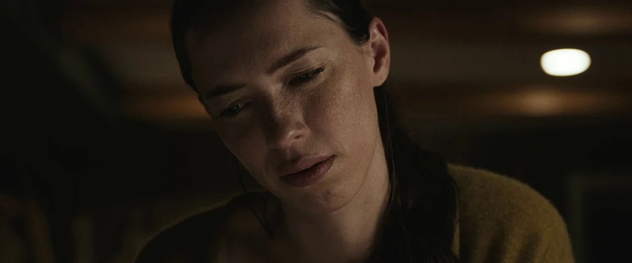 The Night House (2020) movie still: closeup — The frame shows a woman in a dark, dimly lit room. She looks downward with a soft, steady expression.