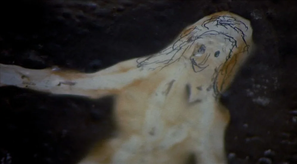 Easy Rider (1969) movie still: closeup — A pale cut-out shape depicting a figure with ink-drawn facial features floats in water. The figure rests…