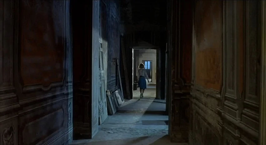 Lisa and The Devil (1973) movie still: wide — An old hallway features dark wooden wall panels and unlit, dusty structural elements. A woman walks…