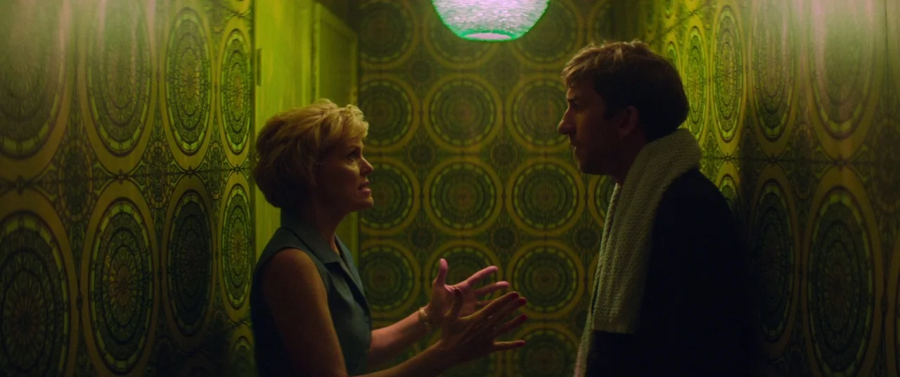 Room For Rent (2017) movie still: medium — A narrow space decorated with repetitive, circular patterned vintage wallpaper in shades of green. A man…