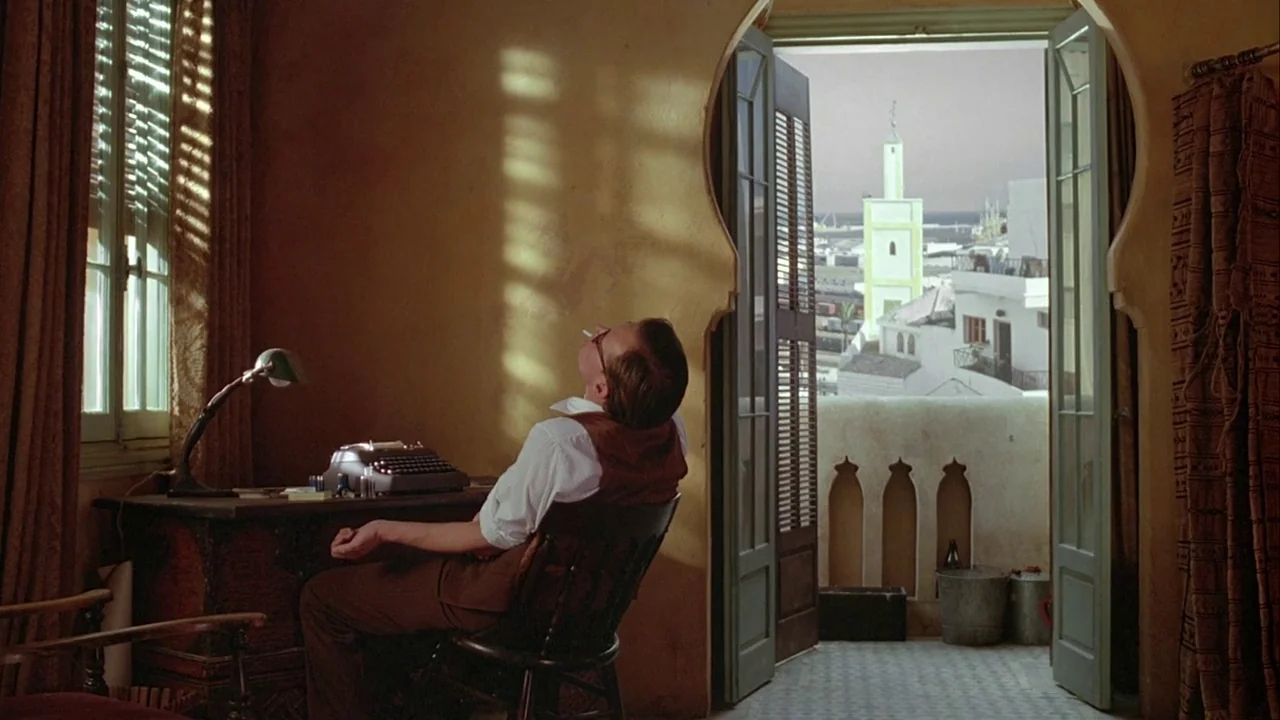 Naked Lunch (1991) movie still: medium — A 1940s study features a desk, typewriter, and open arched doorway leading to a balcony. A man leans back…