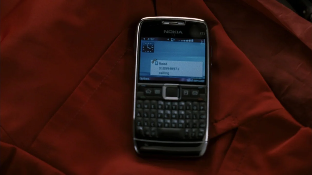 F Valentine's Day (2026) movie still: closeup — A dark red fabric surface provides a background for a small electronic device. A Nokia E71…