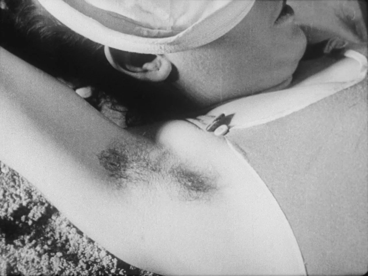 Un Chien Andalou (1929) movie still: closeup — A person lies on sandy terrain while wearing a white tank top and hat. The subject rests with their…