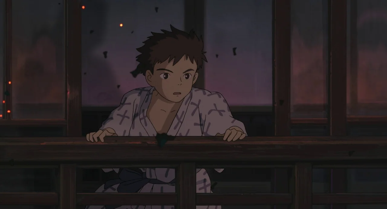 The Boy and The Heron (2023) movie still: medium — A wooden veranda overlooks a dark, smoke-filled night landscape with faint embers flying. A young…