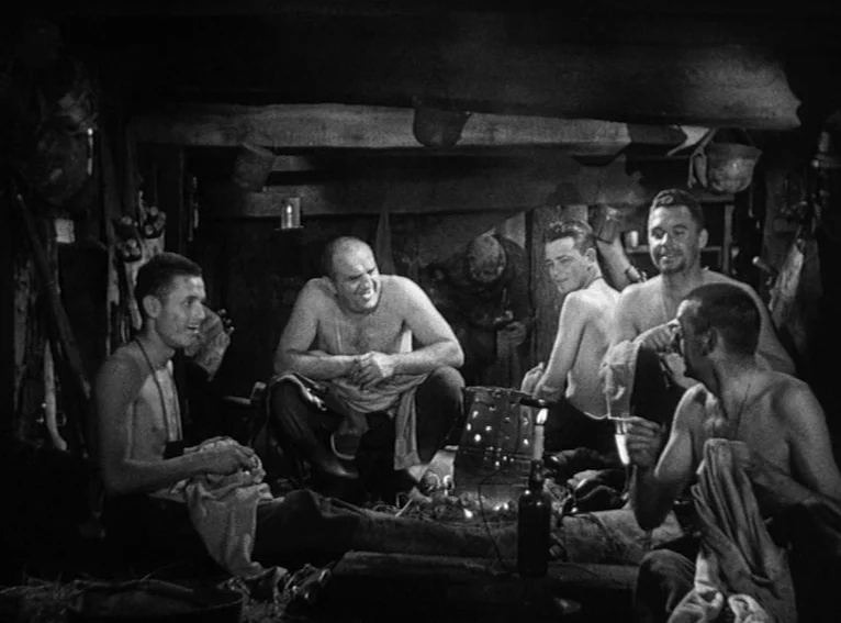 All Quiet on the Western Front (1930) movie still: medium — A dim, enclosed wooden dugout with soldiers resting after duty. Five men sit in a circle…