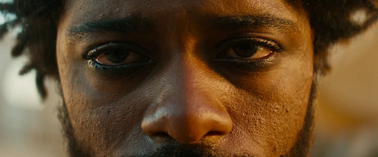 The Book of Clarence (2023) movie still: closeup — An extreme close-up of a man's face set against an out-of-focus outdoor environment. The subject…