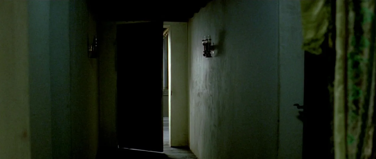 Girl with a Pearl Earring (2003) movie still: establishing — A dark, narrow corridor features smooth walls and a single open door. A small…