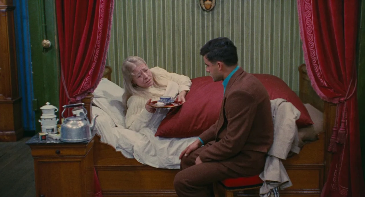 The Umbrellas Of Cherbourg (1964) movie still: medium — An interior bedroom features a wooden bed frame covered with heavy red velvet curtains. A…