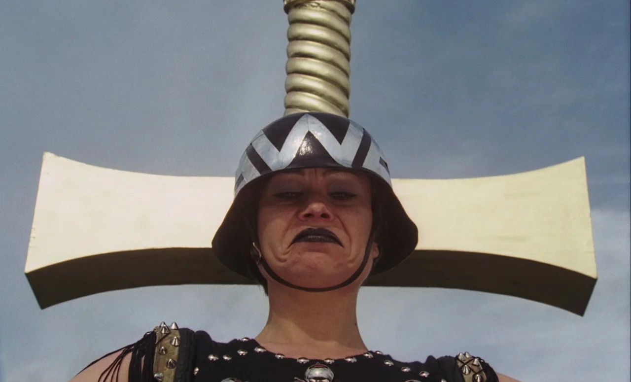 Mahler (1974) movie still: closeup — An open outdoor area features a pale sky and a large gold-colored prop. A woman wearing a futuristic metallic…