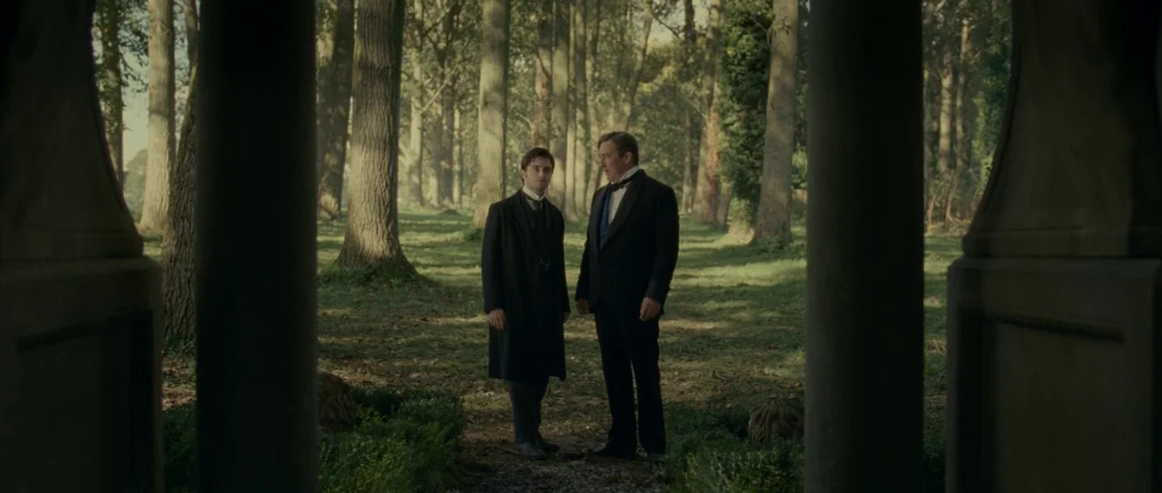 The Woman in Black (2012) movie still: fullbody — A clearing surrounded by a dense line of trees in a woodland area. Two men in formal vintage…