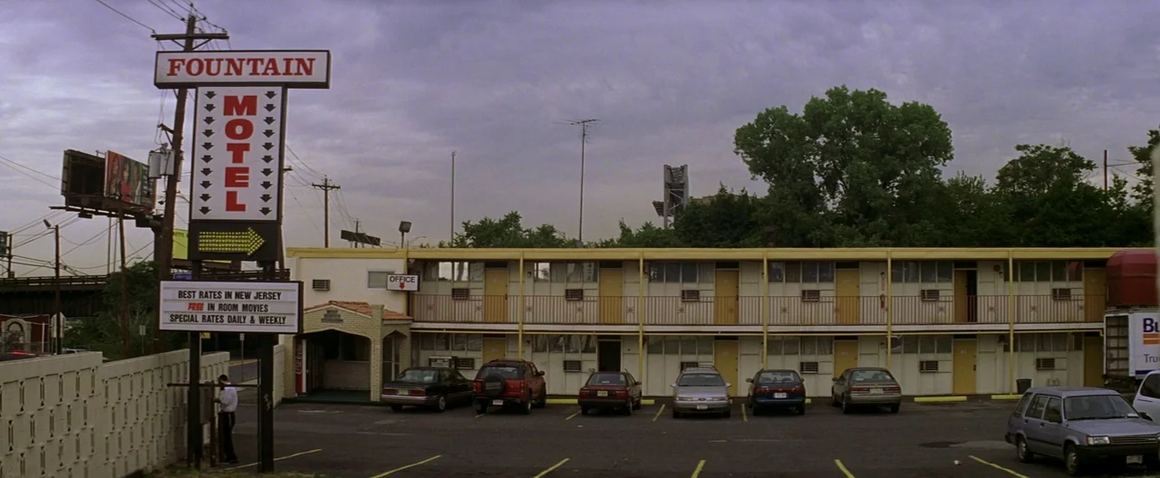 The Yards (2000) movie still: wide — A low-rise two-story budget motel features a long balcony and a parking lot. A prominent roadside sign stands…