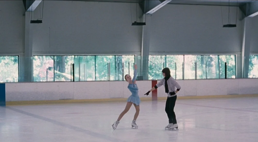 Somewhere (2010) movie still: wide — A spacious, brightly lit indoor ice skating rink features long windows along the back. Two young figure skaters…