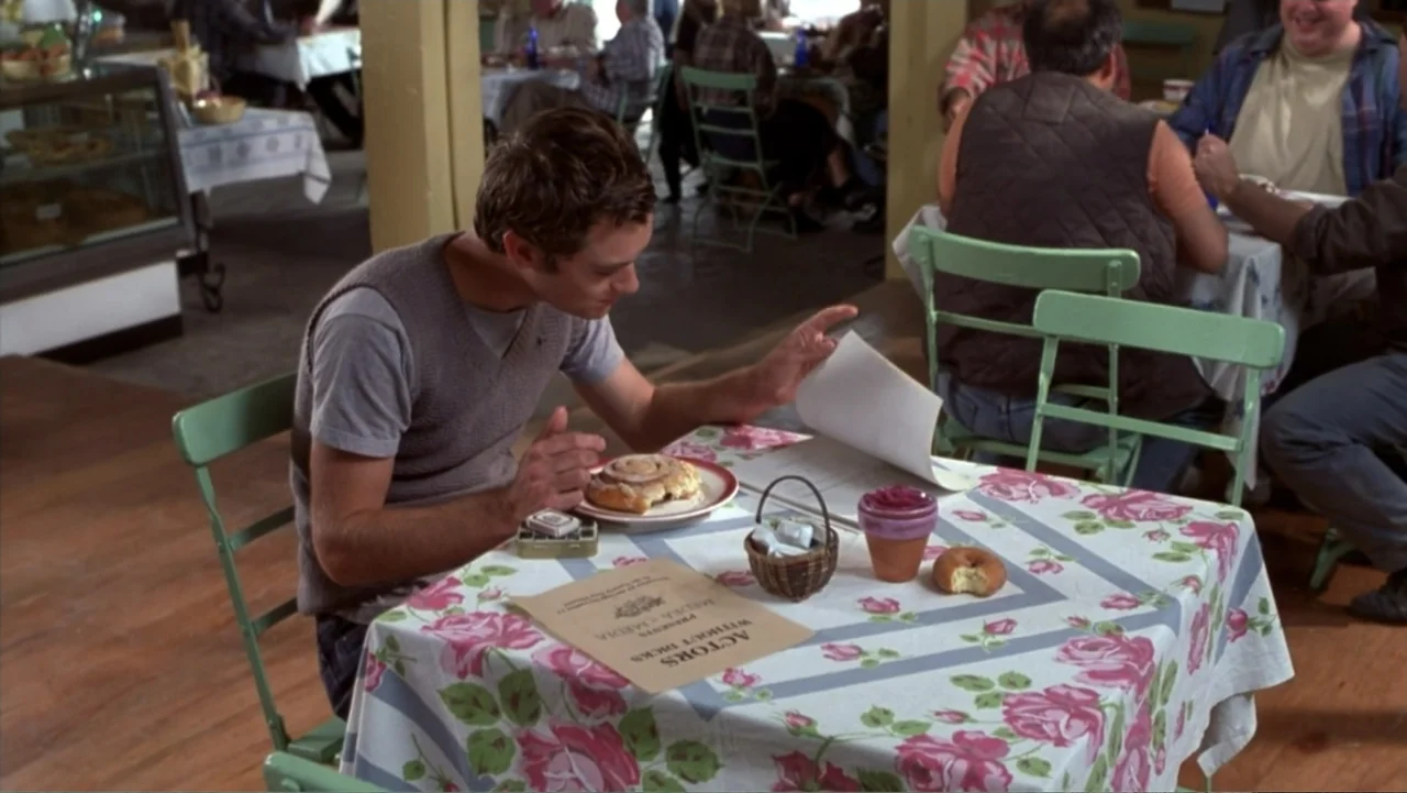 Music from Another Room (1998) movie still: medium — A casual dining space with wooden floors features tables draped in rose-patterned tablecloths.…