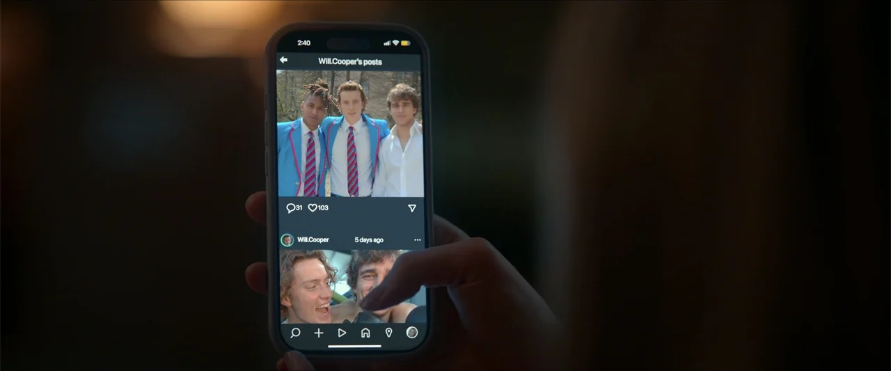 Love Me Love Me (2026) movie still: closeup — A dark indoor setting features a person holding a smartphone in their hand. The screen displays a…