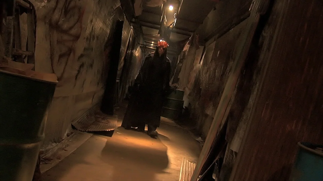 Tokyo Gore Police (2008) movie still: fullbody — A narrow corridor features graffiti-covered concrete walls and several metal barrels along the…