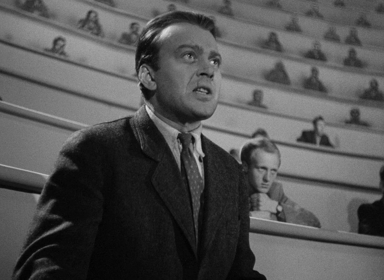 Krakatit (1948) movie still: medium — A tiered lecture hall with many students seated in rows behind a central speaker. A man in a dark suit stands…