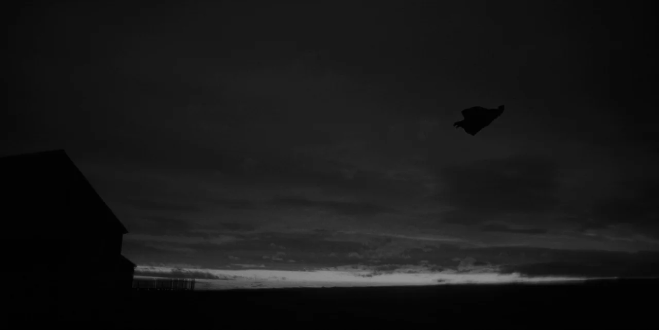 El Conde (2023) movie still: establishing — A dark silhouette of a structure sits on the left of an open field. A small indistinct object is…