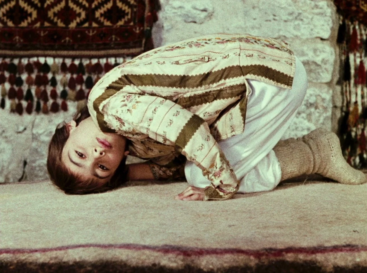 The Colour of Pomegranates (1969) movie still: medium — An interior space features stone walls covered by hanging patterned rugs and tassels. A…