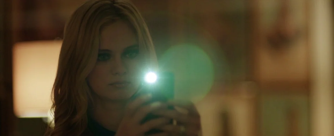 Cheap Thrills (2013) movie still: closeup — A dimly lit interior room at night provides a shadowy, low-visibility environment. A young blonde woman…