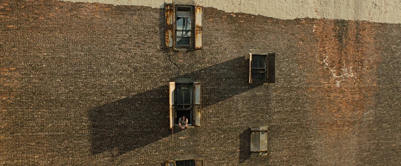 Across the Universe (2007) movie still: wide — A tall, weathered dark brick wall features several windows with worn wooden shutters. A solitary…