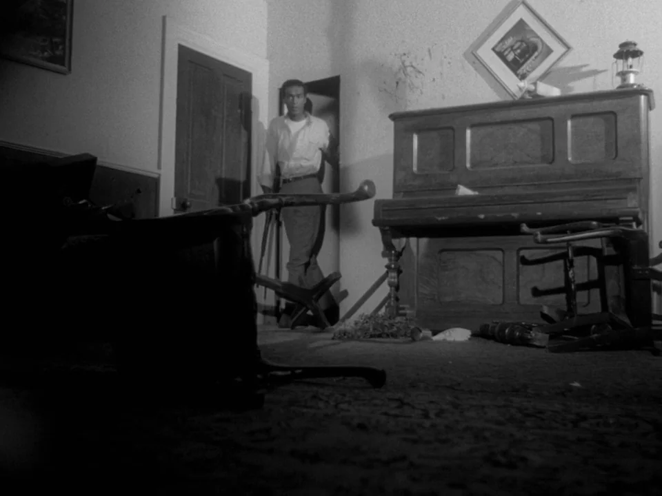 Night of the Living Dead (1968) movie still: fullbody — A cluttered room contains an upright piano and overturned furniture scattered across the…