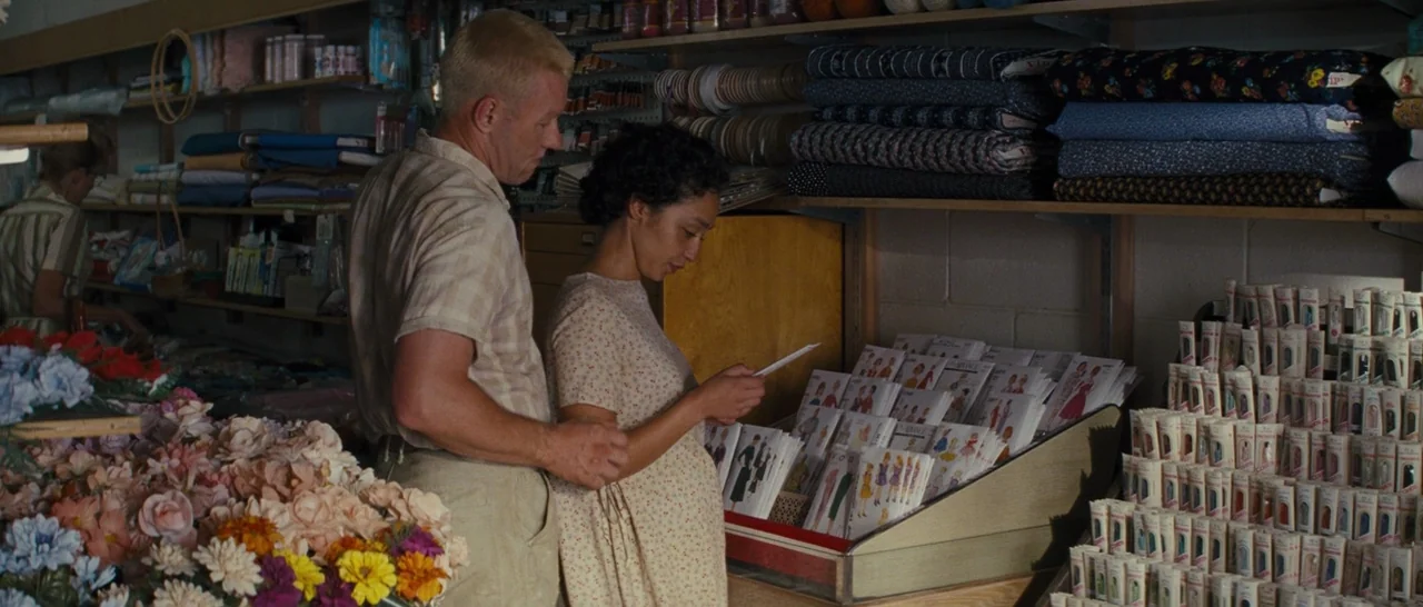 Loving (2016) movie still: medium — An interior fabric store with shelves of textile bolts and sewing patterns. A man and a pregnant woman stand…