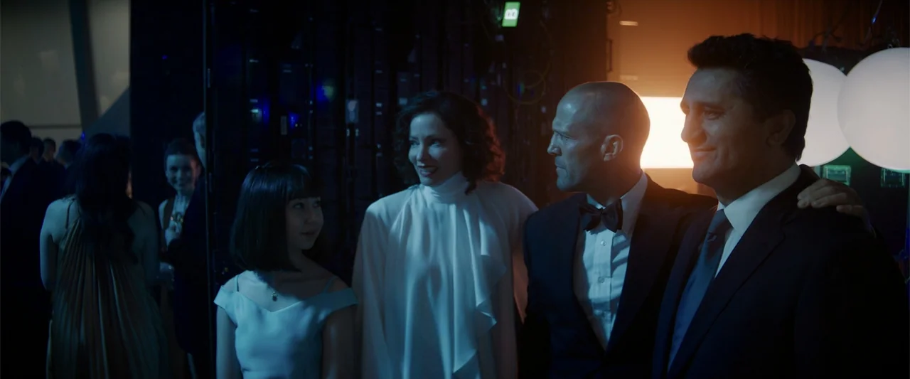Meg 2: The Trench (2023) movie still: medium — A dimly lit room holds a gala with people in formal attire and glowing orbs. Four individuals stand…