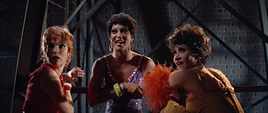 Sweet Charity (1969) movie still: medium — A dark, brick-walled industrial space with exposed metal beams and girders. Three women in theatrical…