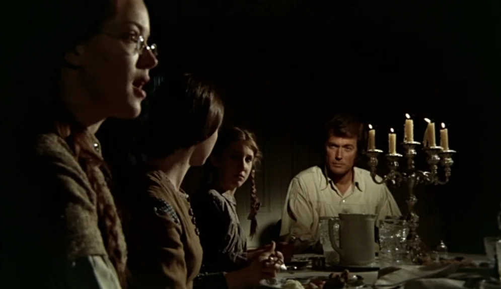 The Beguiled (1971) movie still: medium — A group of people are seated at a wooden table in a dimly lit room. The man sits opposite the women while…