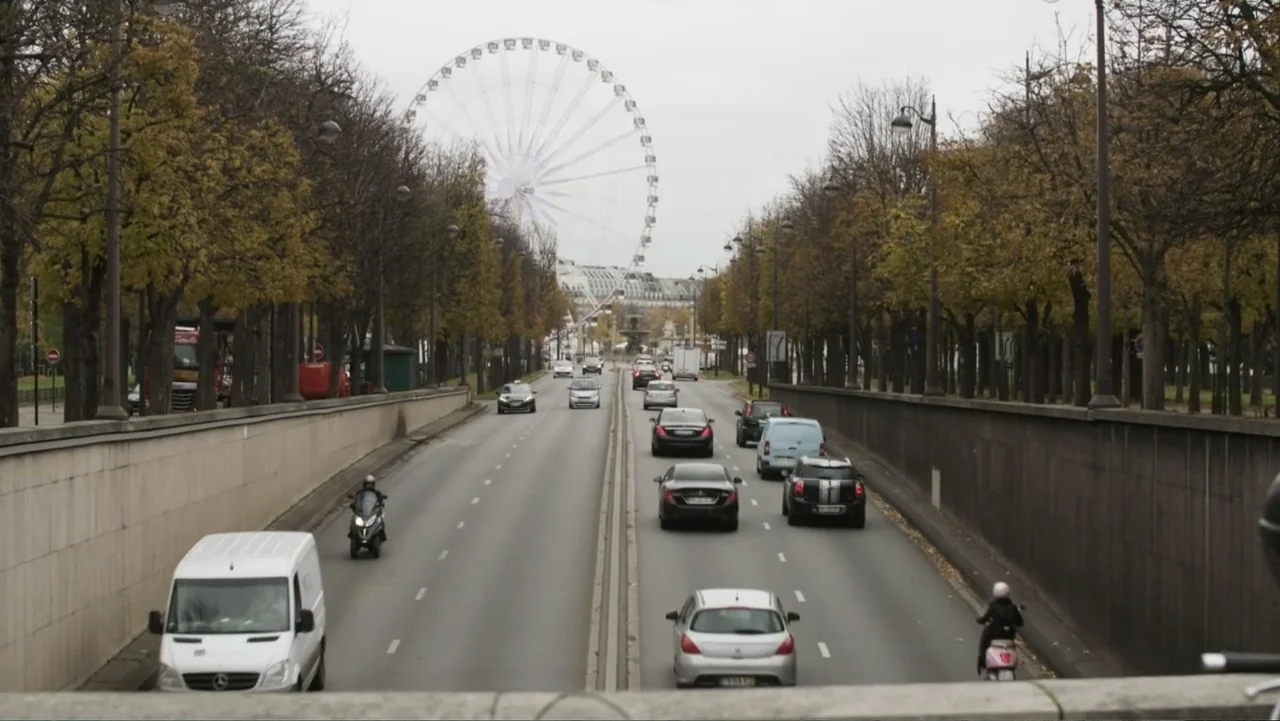 The FIFA Family: A Love Story (2017) movie still: establishing — An urban road runs through a concrete underpass with bare trees lining the banks.…