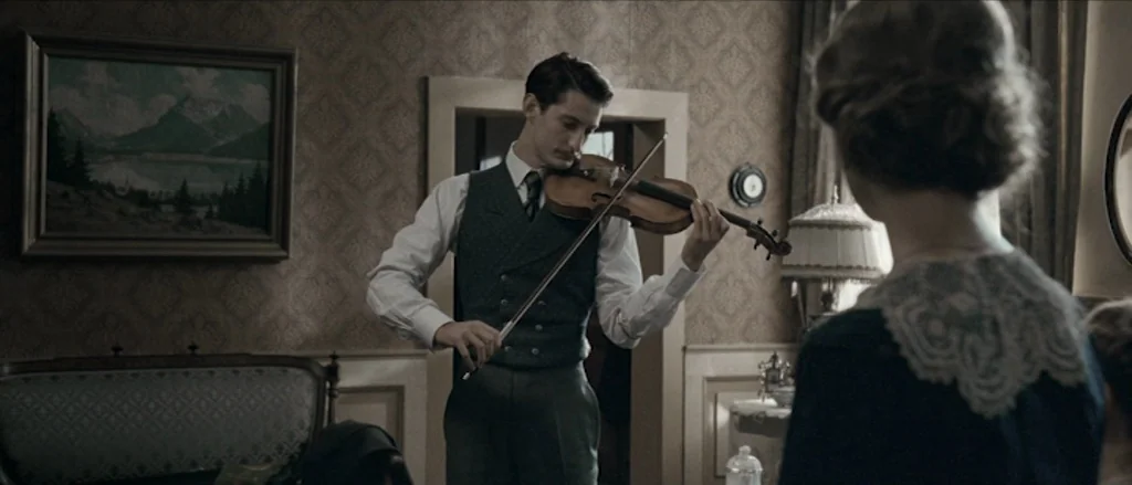 Frantz (2016) movie still: medium — A 1940s domestic interior features patterned wallpaper and a framed landscape painting. A man in a vest plays…