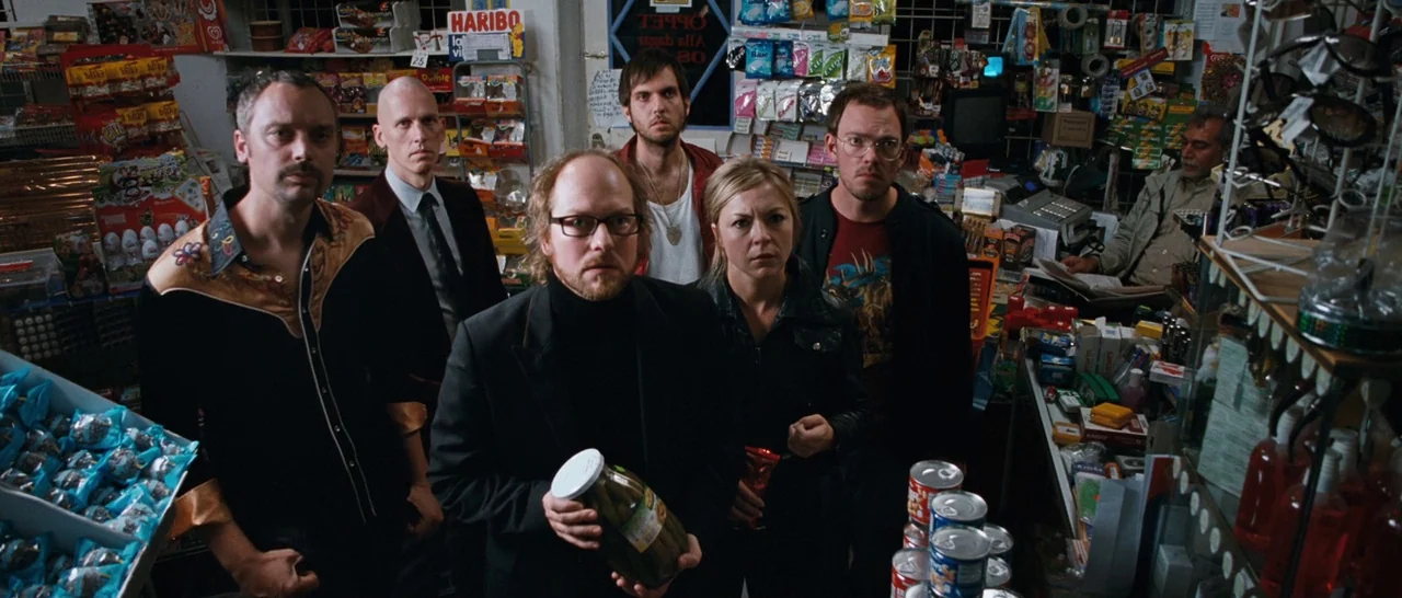 Sound of Noise (2010) movie still: medium — A cluttered small convenience store filled with racks of snacks and grocery items. Five people stand in…