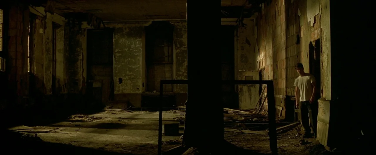 The Yards (2000) movie still: wide — A dilapidated, empty room features rotting debris and peeling paint on the dark walls. A young man stands in…