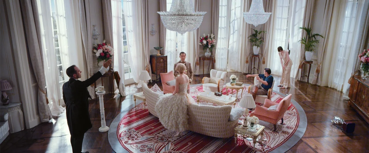 The Great Gatsby (2013) movie still: wide — An opulent, high-ceilinged drawing room features large white curtains, crystal chandeliers, and parquet…
