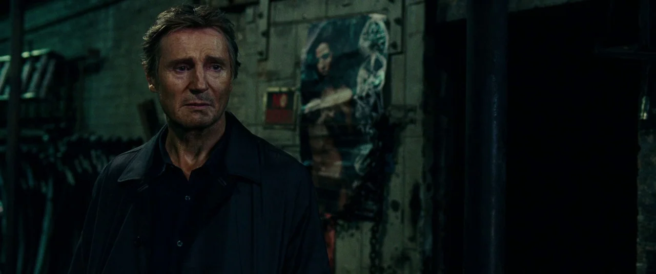 Widows (2018) movie still: medium — A dimly lit industrial basement features dark brick walls and shadowy corners. A man in a dark coat stands in…