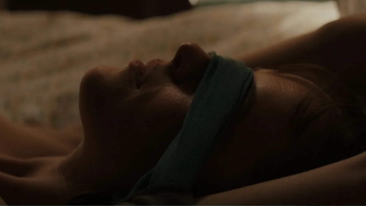 Fifty Shades of Grey (2015) movie still: closeup — A close-up view shows a person resting in a darkened room with fabric bedding. A woman lies on…