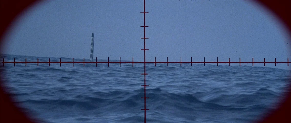 The Hunt for Red October (1990) movie still: wide — A dark blue ocean surface extends toward a hazy horizon line under overcast skies. A submarine…