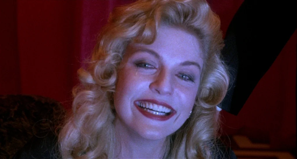 Twin Peaks: Fire Walk With Me (1992) movie still: closeup — A woman stands before a dark red curtain in a dim, surreal space. The woman stares…