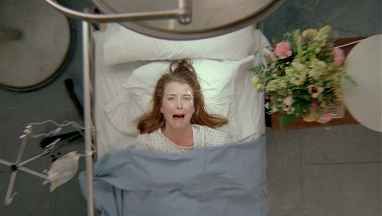 Necronomicon: Book of Dead (1993) movie still: medium — A hospital room contains a bed, an IV pole, and a bouquet of flowers. A woman lies in the…
