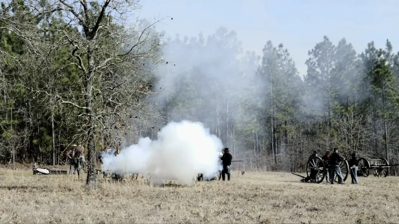 Kill Cavalry (2021) movie still: wide — A group of men in 19th century attire stand in an open field. They are firing a large antique field cannon…