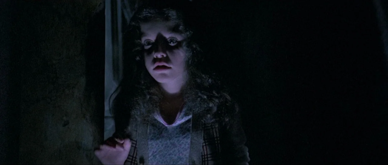 Opera (1987) movie still: medium — A dark, underexposed interior space surrounds the subject on all sides. A young girl is illuminated from below by…