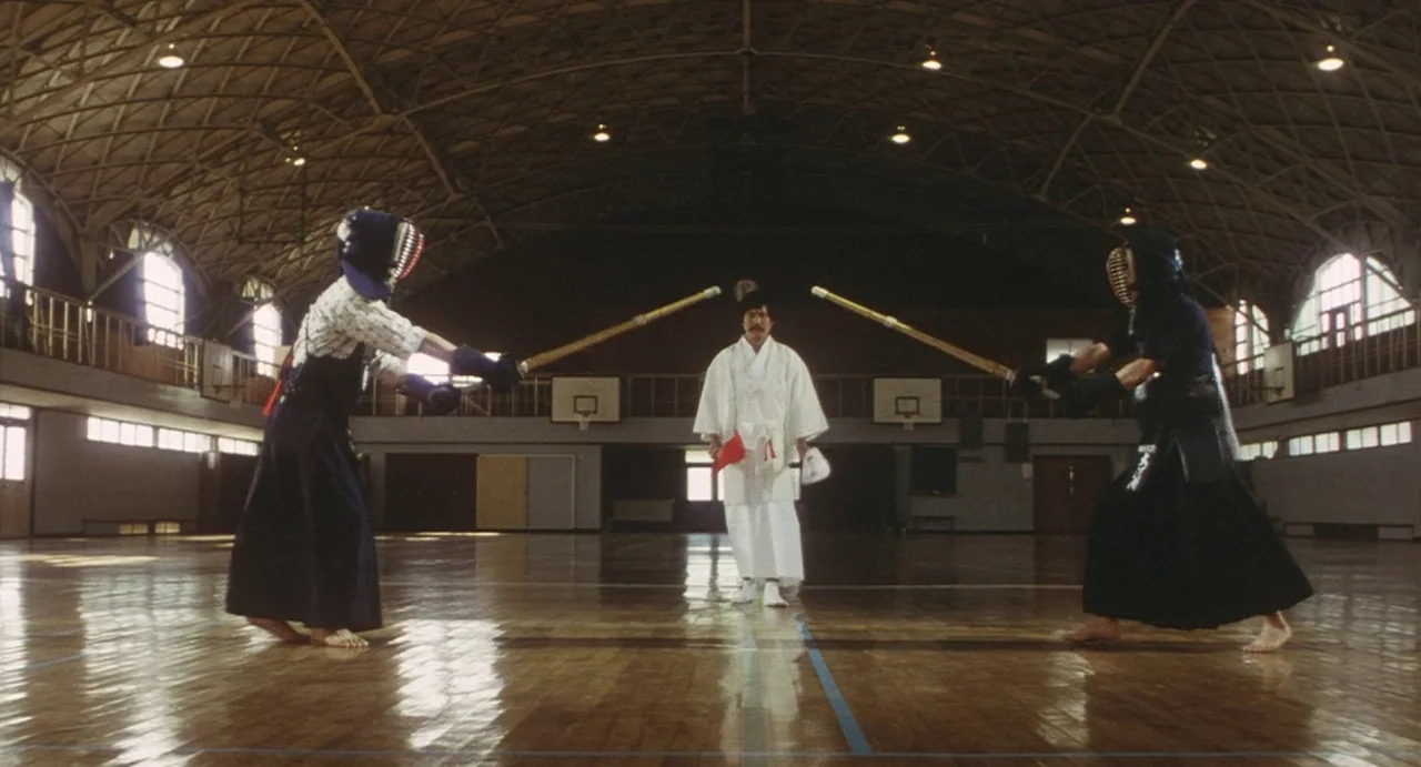 School in the Crosshairs (1981) movie still: fullbody — A wooden gymnasium with a vaulted arched ceiling and large arched side windows. Two people…