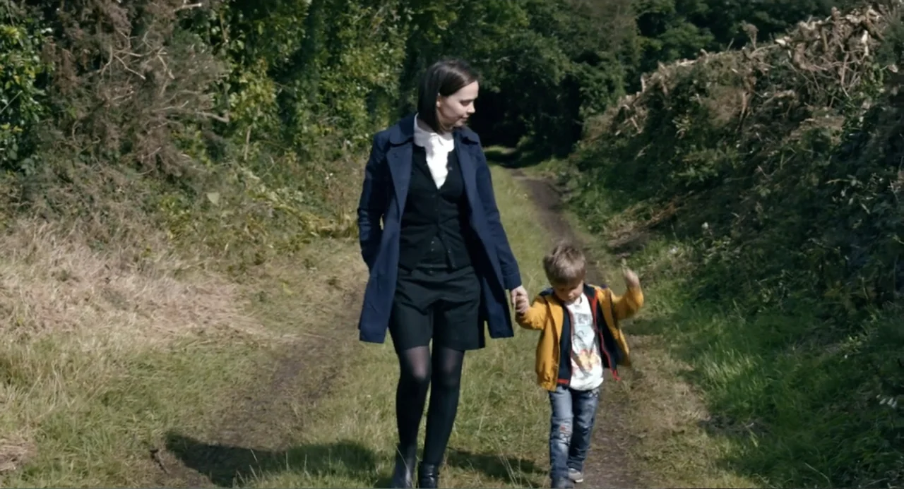Living Out Loud (1998) movie still: fullbody — A dirt path flanked by dense green foliage and tall grass under soft sunlight. An adult woman walks…